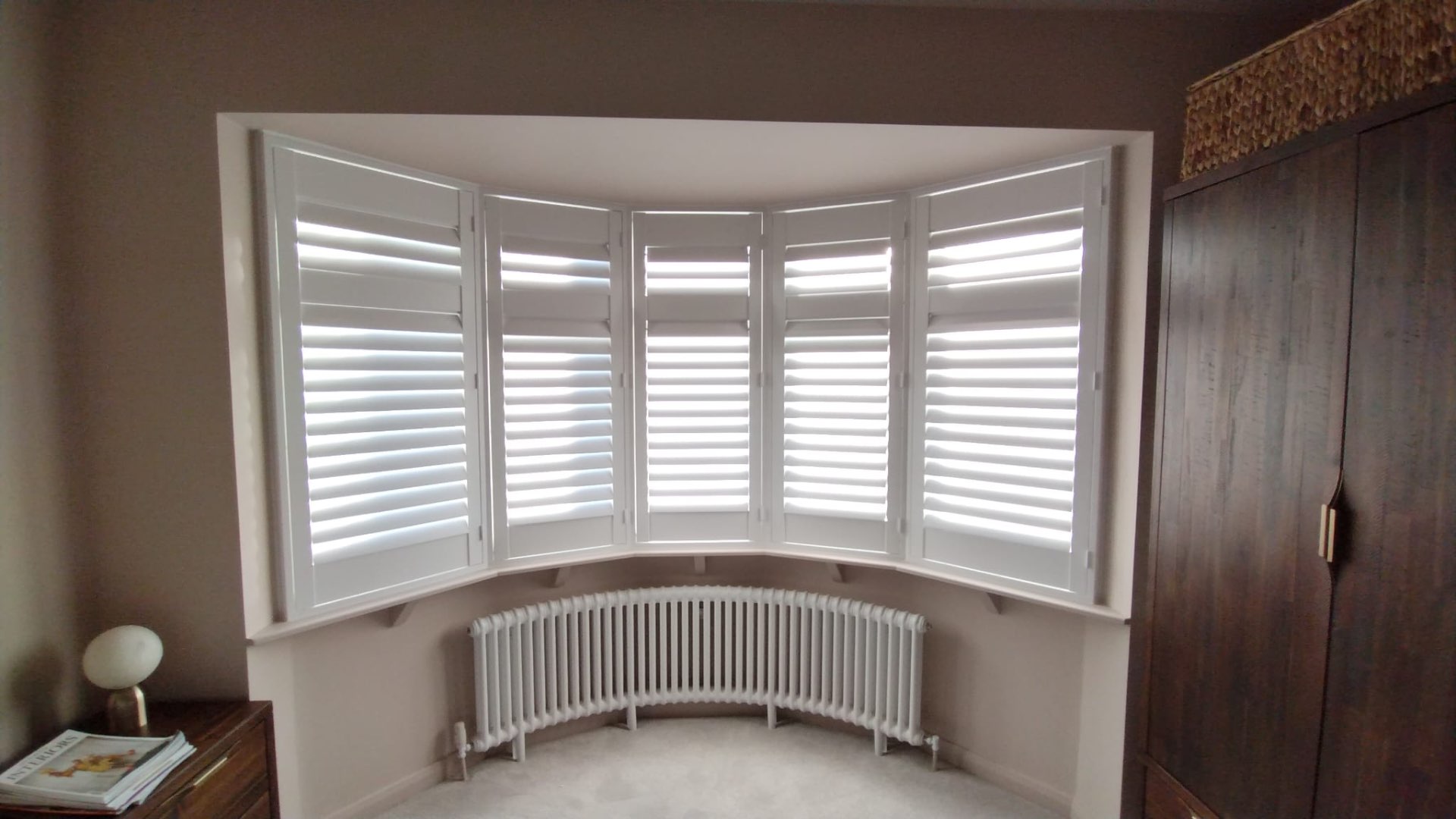 Full-height white plantation shutters in a bay bedroom window